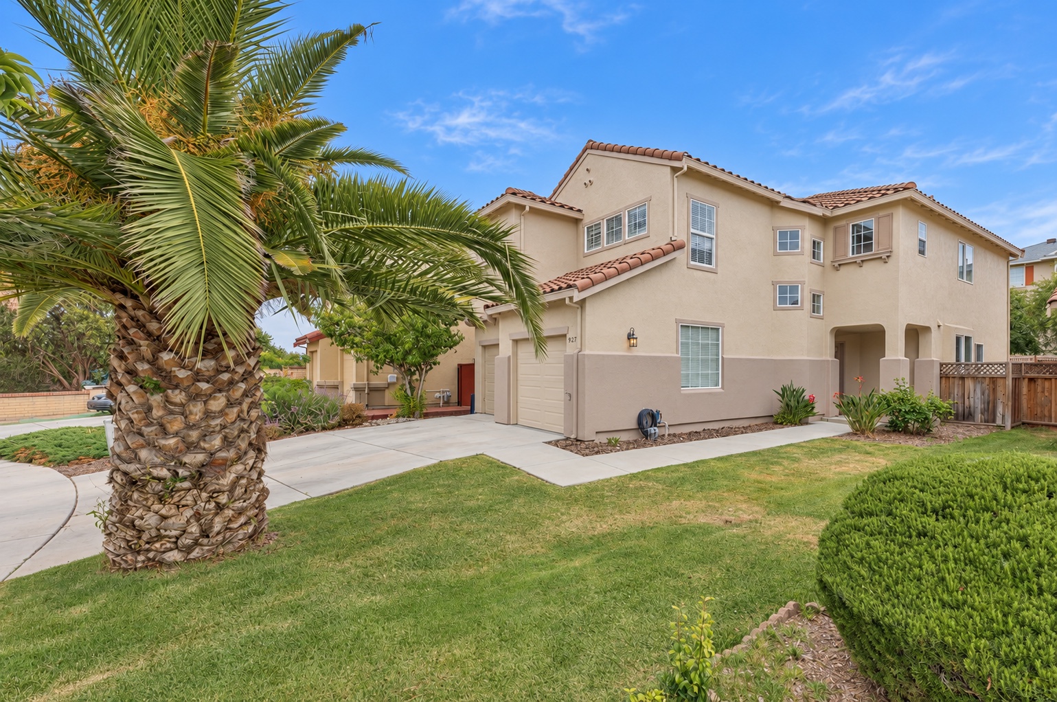 A two-story stucco home with a tiled roof, palm tree, lawn, and landscaped front yard.